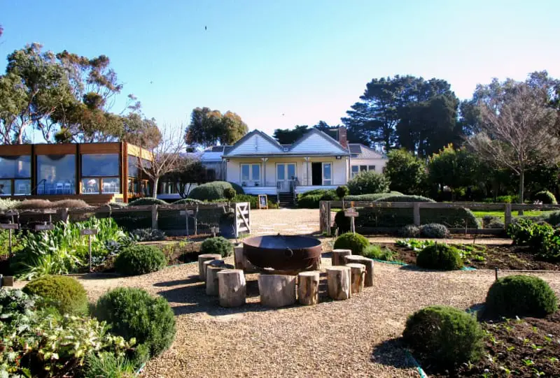 View of Basil's Farm winery on the Bellarine Peninsula with a fire pit and gardens, trees, and blue sky.