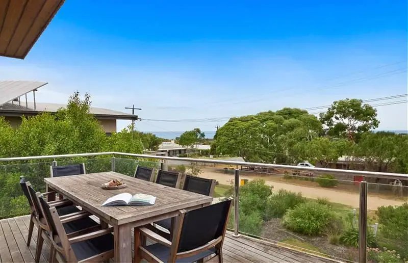 Balcony with outdoor furniture overlooking trees and the ocean at Beach Road Luxury with Ocean Views holiday accommodation in Aireys Inlet.