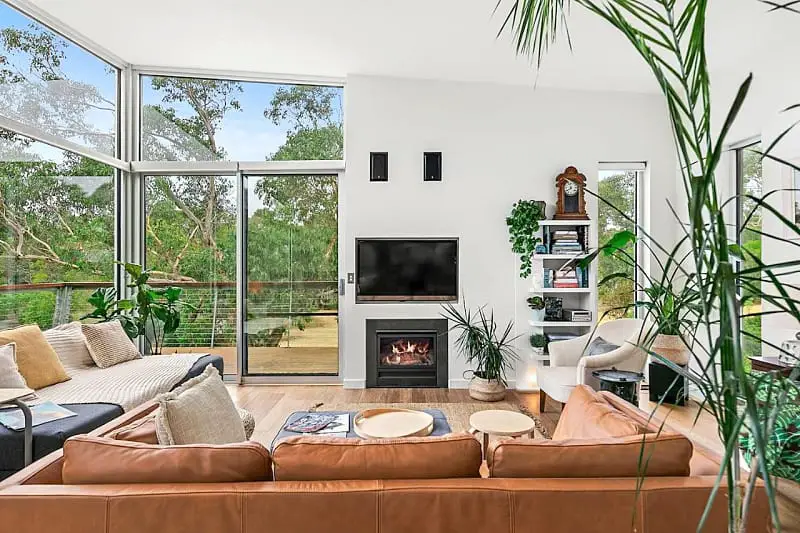 Living room with couches, a television, and large windows with garden views at Bristlebird Aireys Inlet holiday accommodation.