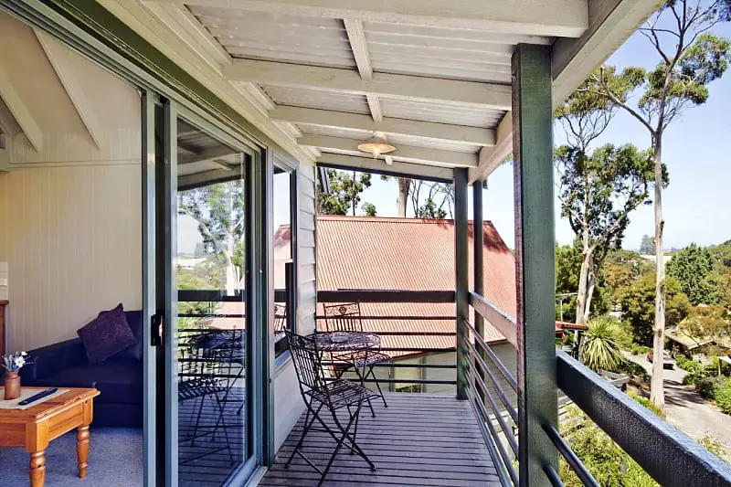 Balcony with table and chairs and open sliding door leading into the living area of guest accommodation Great Ocean Road Cottages in Lorne.