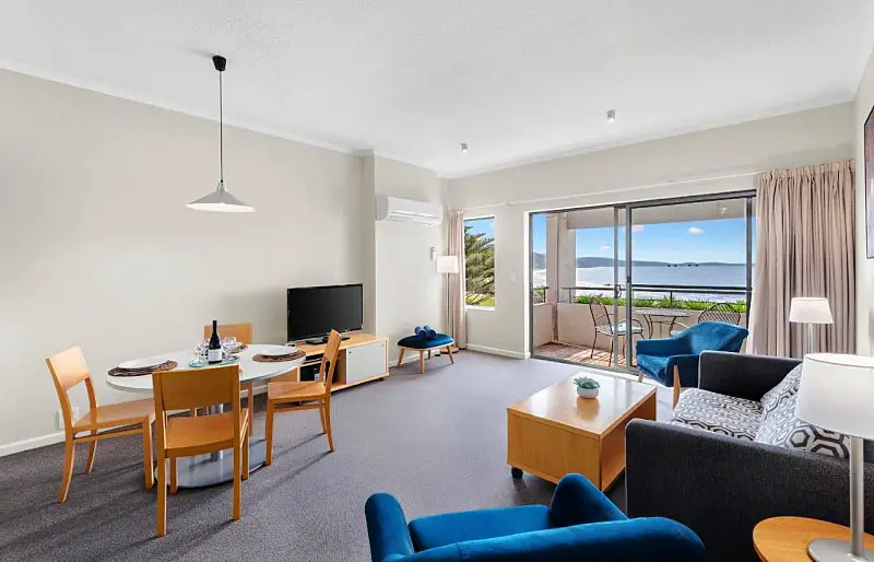 Living room with a television, dining table, and couches at Lorne Beach and Louttit Bay View apartment at the Cumberland Lorne accommodation.