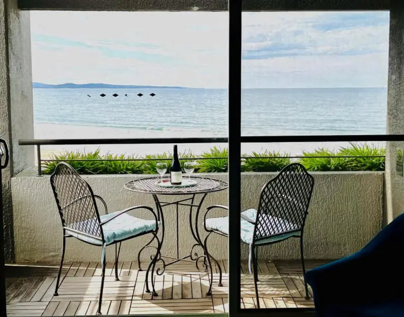 View through a guest room window to a balcony with outdoor setting overlooking the beach at Lorne Beach and Loutitt Bay View apartment at the Cumberland.