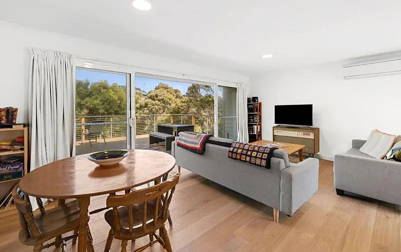 Open plan living area with dining table and couches and sliding doors that open to a deck at Myrtle Cottage in Aireys Inlet.