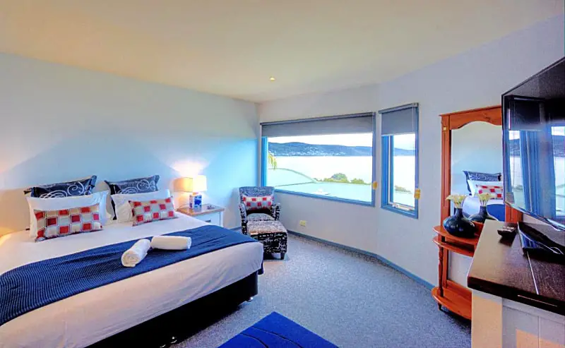 Guest bedroom with a bed, chair, dresser, and large windows with ocean views at Pierview holiday accommodation Lorne.