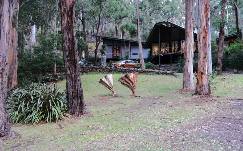 View of the accommodation at QDOS Tree House Lorne accommodation surrounded by trees with a car and an art sculpture in the foreground.