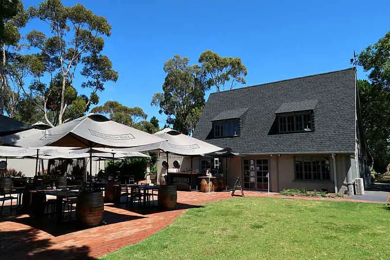 The A-frame shaped cottage style cellar door and alfresco dining area with umbrellas, blue skies, trees and lawn area at Scotchmans Hill Bellarine winery.