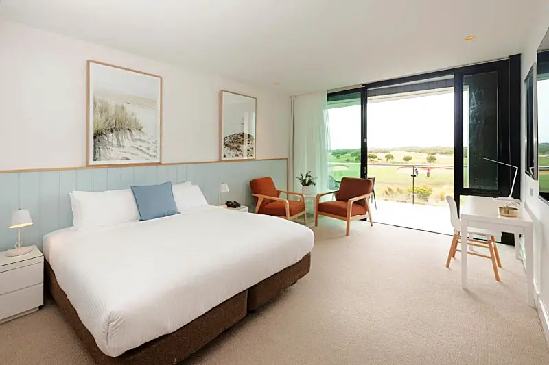 Guest room at The Sands Resort in Torquay with a bed and sitting area and balcony overlooking the golf course.
