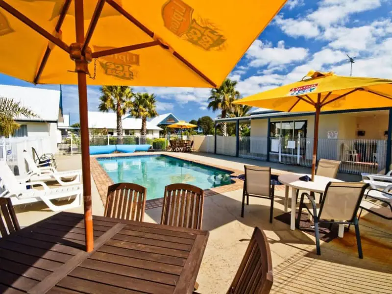 Pool area with picnic tables and bright yellow umbrellas at the Torquay Tropicana Motel.
