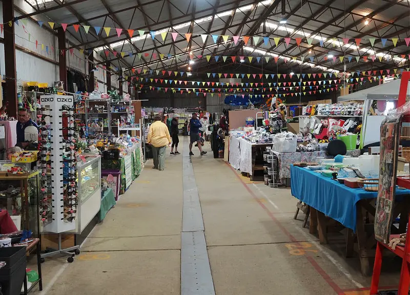 Market stalls at the Warrnambool Sunday Undercover Market with customers shopping and colourful bunting strung up on the ceiling.