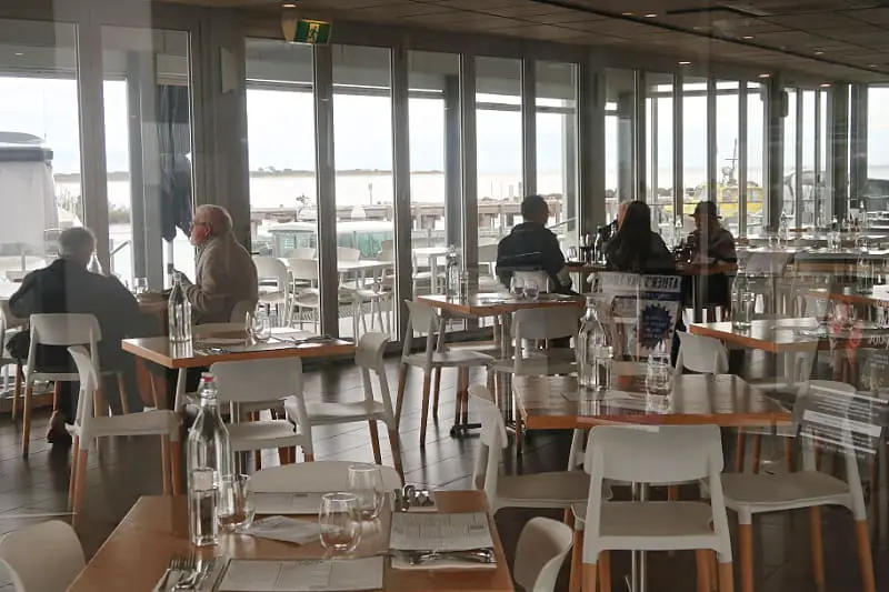 Dining room at 360Q restaurant in Queenscliff. There are large windows overlooking the harbour and people sitting enjoying a meal.