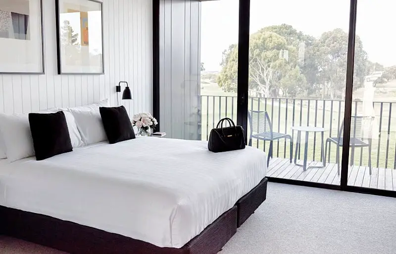 Accommodation@Curlewis guest room a handbag sitting on the bed and glass sliding doors with views of the balcony and outdoor furniture and golf course with trees.