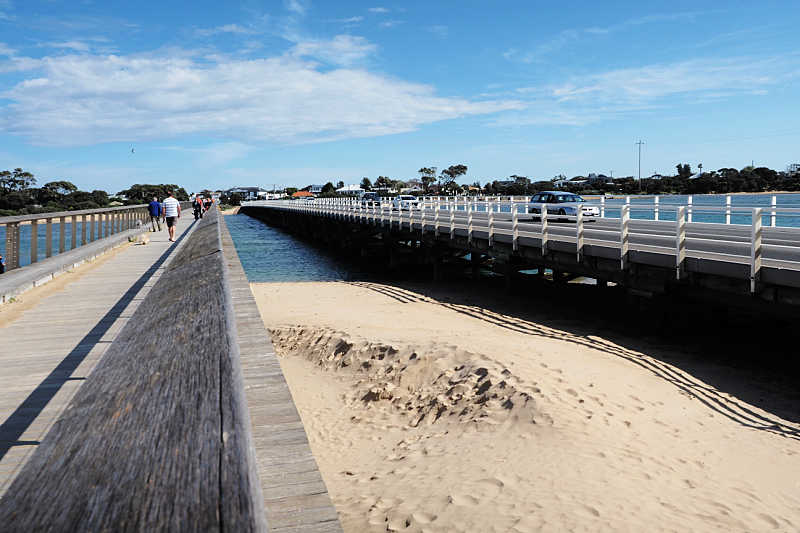The two bridges at Barwon Heads that connect to Ocean Grove Victoria. People are walking across one bridge and there are cars crossing the other bridge. 