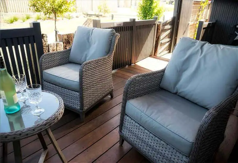 Outdoor decking with comfortable cane chairs with cushions and a table with wine glasses at Bellarine Getaway.