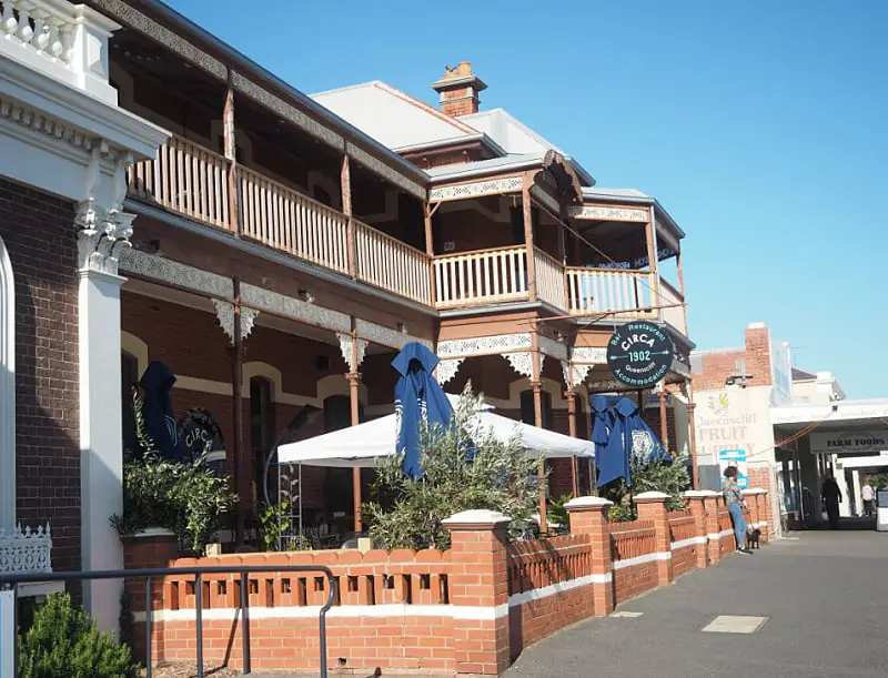 Woman leaning against the brick fence of the Circa restaurant courtyard. There are umbrellas in the front courtyard, an upstairs verandah, and a round sign saying Circa 1902. 