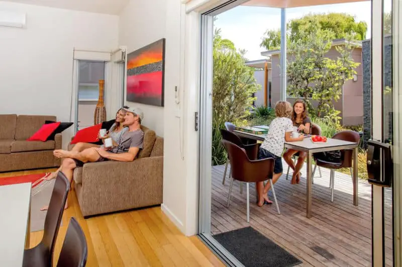 People relaxing inside and on the verandah a cabin at Ingenia Queenscliff caravan park accommodation.