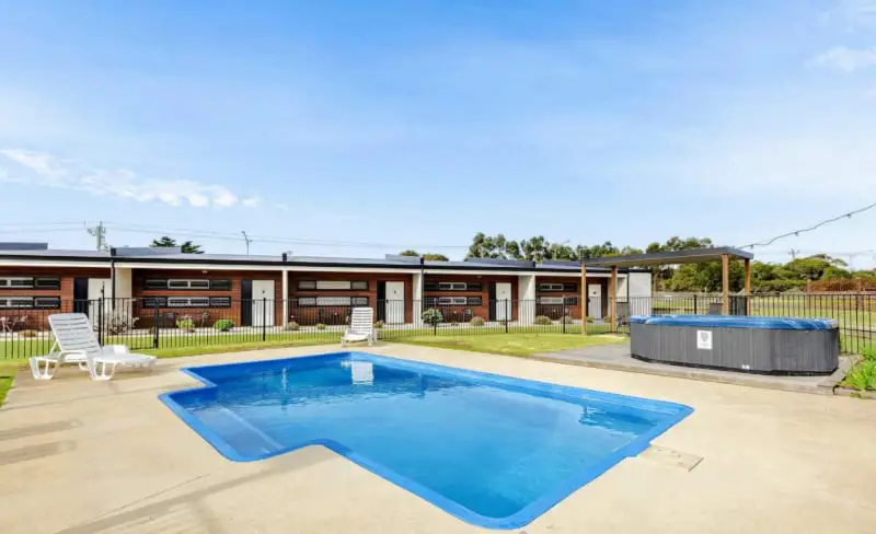 View of the pool and outdoor spa area with white lounge chairs and motel rooms in the background at Lakeview Hideaway accommodation on the Bellarine Peninsula in Victoria.