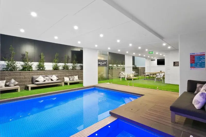 Bright blue indoor swimming pool area with fake grass and sun lounges at Ocean Grove Chalet.