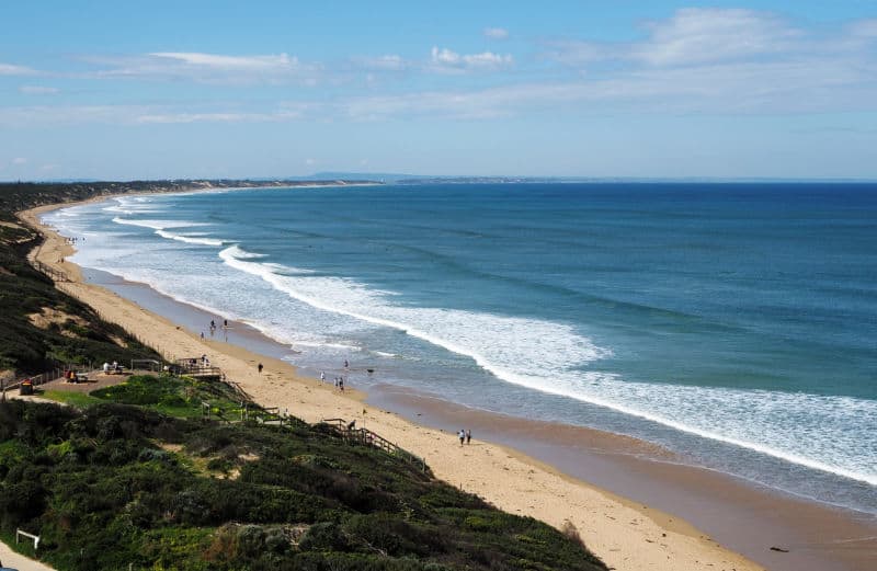 View of people walking on the long beach and ocean with gentle white capped waves at Ocean Grove in Victoria Australia.