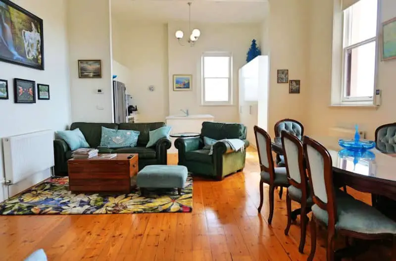 Guest living room at Ozone Tower accommodation in Queenscliff Victoria. It has polished floorboards, a dining table and chairs, a lounge suite, coffee table, and a rug. 