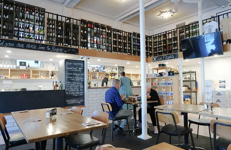 Two men sitting at a table and a woman ordering at the bar at Queenscliff Brewhouse a great place for taste testing gin, beer, and wine or for having a meal.