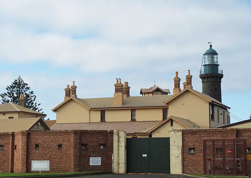 Fort Queenscliff on the Bellarine Peninsula in Victoria surrounded by a brick wall and heavy green gates with views of the Black Lighthouse behind it. A tour of the fort is a great way to learn the history of Australia's 
Denfence Forces. 