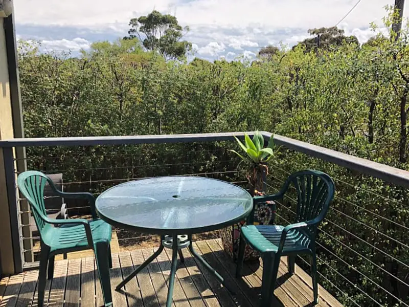 Round outdoor table with two chairs on a balcony overlooking green shrubs at Seagrape Cottage.