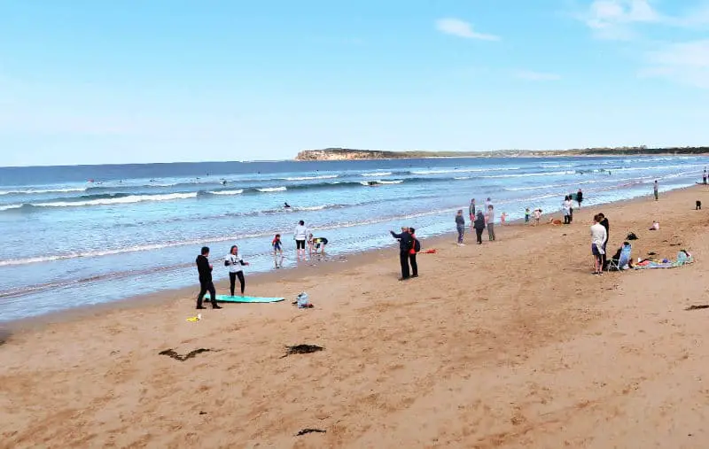 Person having a surfing lesson in Ocean Grove. They are standing on a surf board on the sand with an teacher giving instructions. 