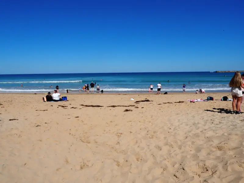 People walking on the shoreline at Surfside beach on a clear blue day.