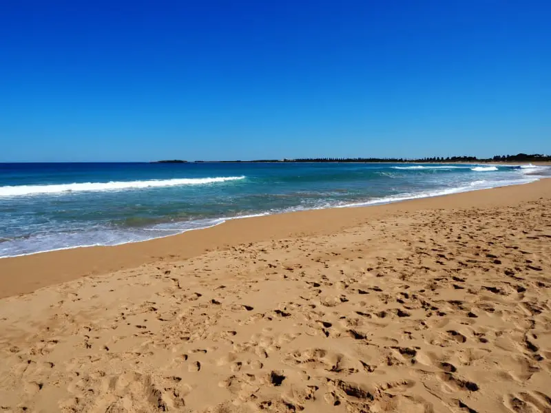 Bright blue skies and gentle white capped waves at the golden sand Flume Beach. One of the beautiful ocean beaches in Warrnambool Victoria.