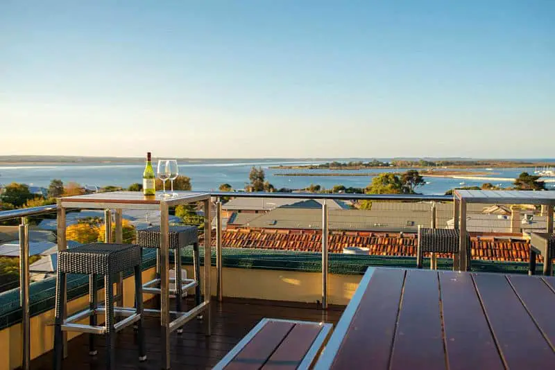 View of the ocean from the rooftop at Queenscliff's Vue Grand Hotel on the Bellarine Peninsula. There is a table with a wine bottle and two glasses sitting on it and chairs.