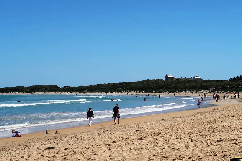 People walking along the shoreline at one of the many Warrnambool Beaches on a clear day with bright blue skies.