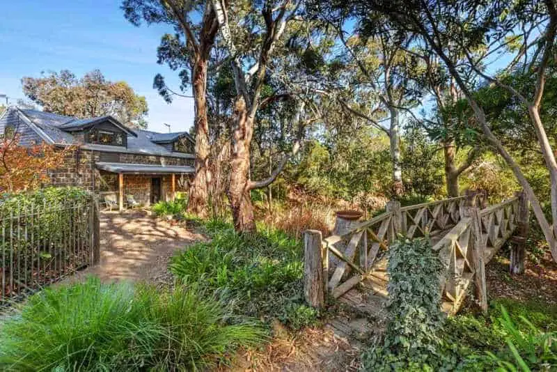 Woodlands Retreat brick cottage and native garden with a small wooden bridge and large eucalyptus trees.