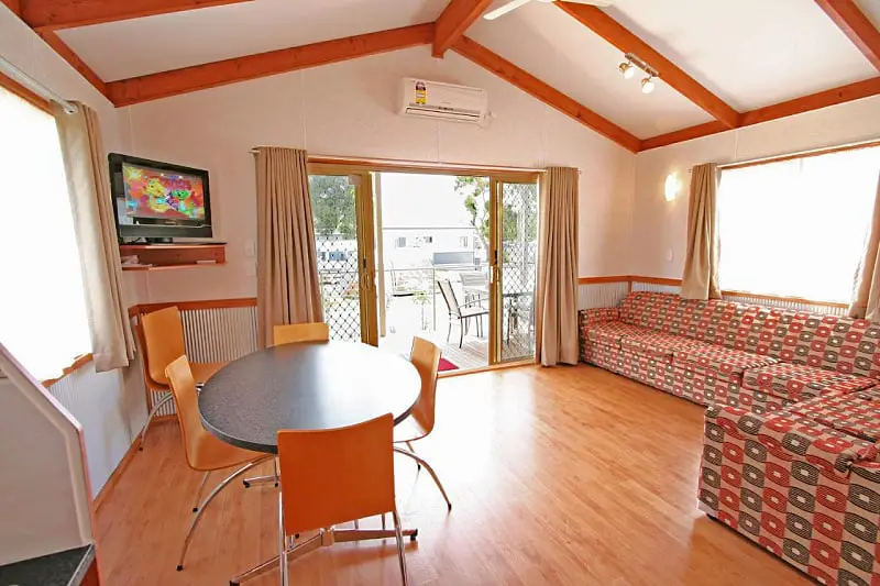 Open plan living and dining with timber look flooring and exposed roof beams in an Apollo Bay Holiday Park cabin. A centrally located Apollo Bay caravan park.