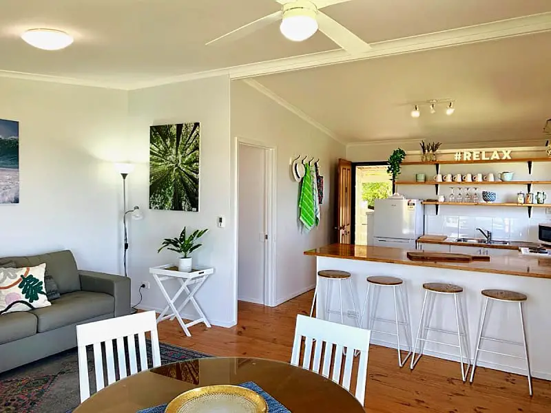 Open plan kitchen, dining, and living area at Apollo Bay Waterfront Motor Inn. There is a kitchen bench with stools, a round dining table and a couch.  