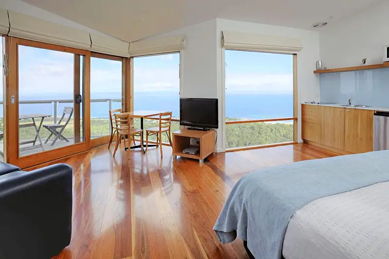 Guest room at Chris's Beacon Point Villas with polished floorboards, a bed, television set and ocean views through floor to ceiling windows. A top choice for Apollo Bay accommodation.
