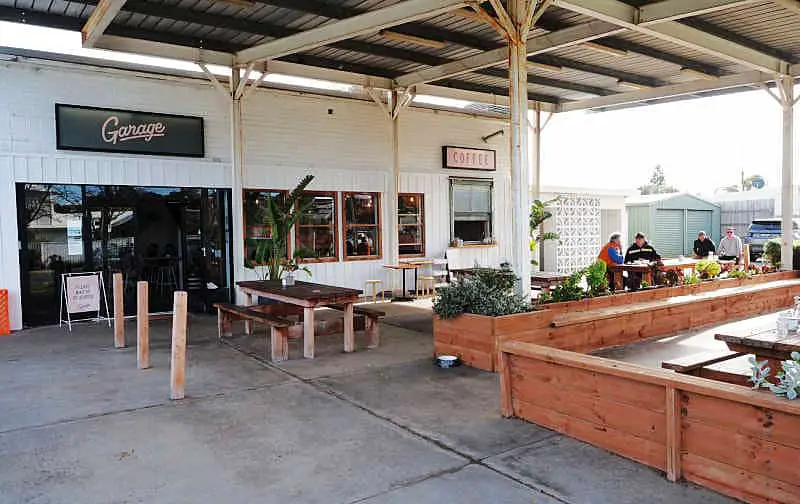 Outdoor dining at Garage Ocean Grove cafe with coffee window, diners, and green plants.