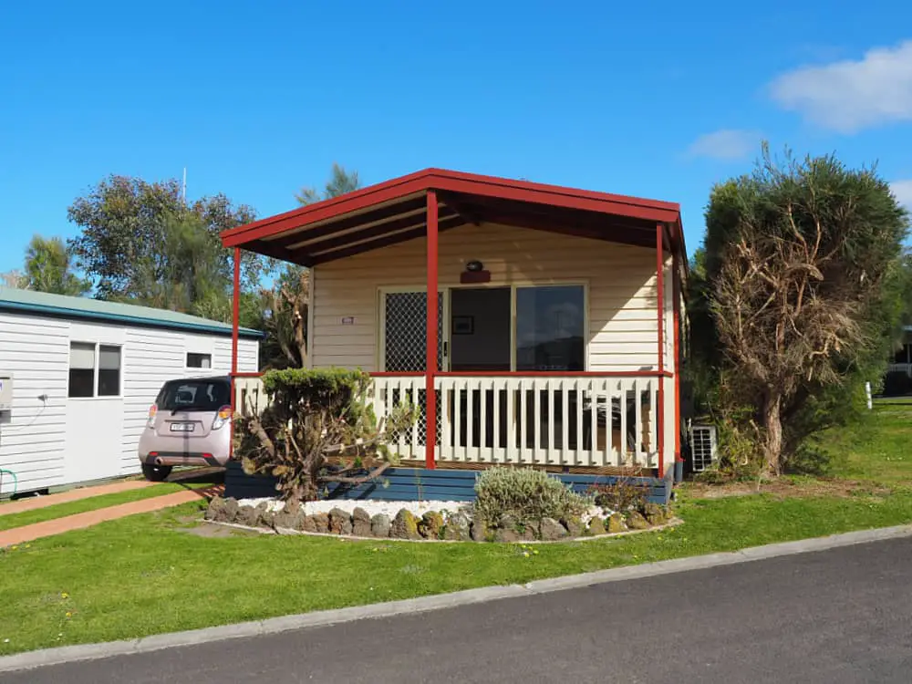 Marengo Caravan Park cabin with a verandah and a small garden. There is a pink car parked in the allocated space beside the cabin.