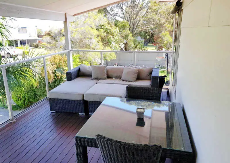 Large deck with a day bed and table and chairs surrounded by greenery at Portarlington Beach Shack.