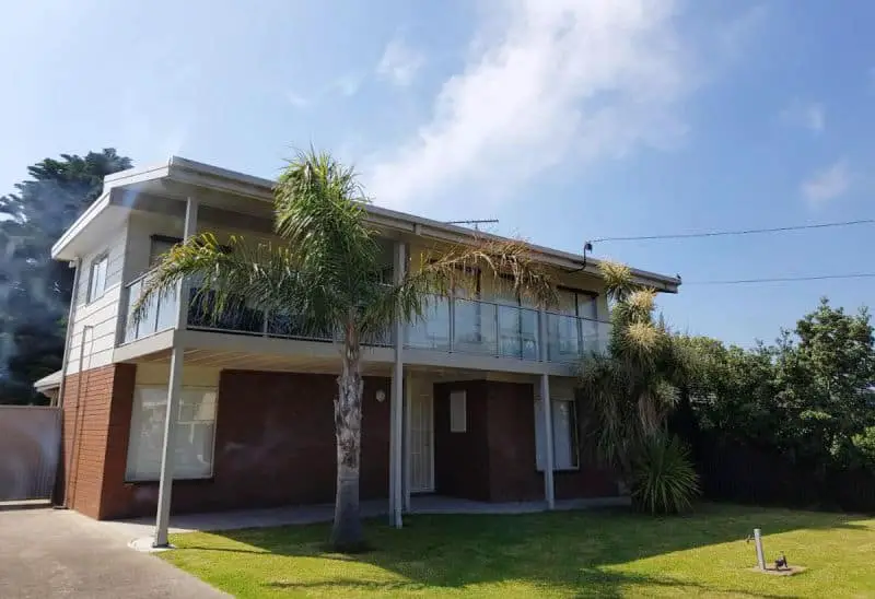 The two storey Portarlington Beach Shack with a verandah and balcony and palm trees out the front.