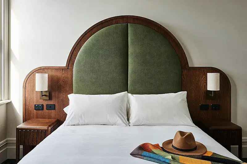 Large bed with a green semi-circle headboard, white linen, and a hat and scarf at Portarlington Grand Hotel guest room. A recommended place to stay in Portarlington. 