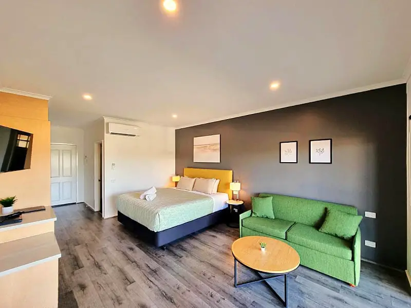 Modern guest room at Seaview Motel & Apartments in Apollo Bay with a queen bed, a green couch, and a coffee table.