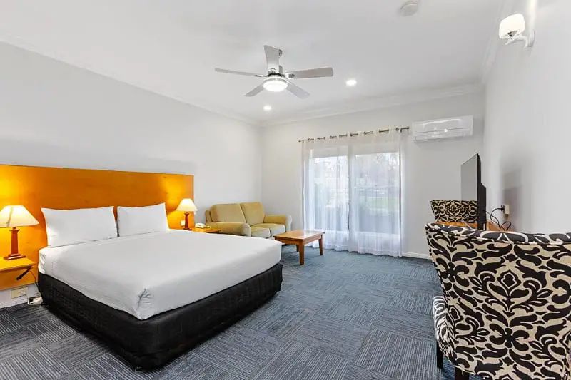 Guest room at The International Apollo Bay hotel accommodation. There is a king bed with timber bedhead, bedside tables and lamps, a small seating area, a TV, and modern highbacked chairs.