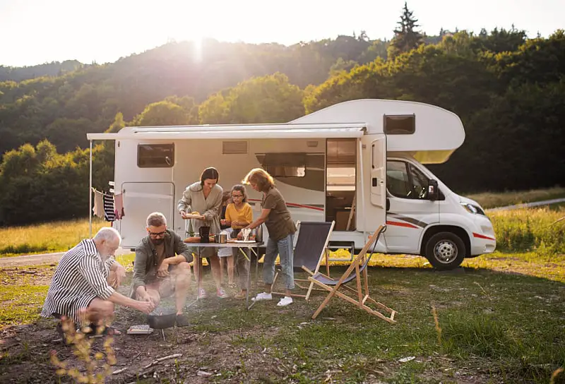 People cooking a meal on a camp fire beside a parked motorhome. Camping in a motorhome is a popular way to travel on the Great Ocean Road in Victoria. 