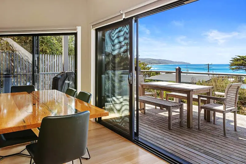 Partial view of the dining table at Achilles holiday accommodation in Apollo Bay. A decked area with outdoor setting and southern ocean can be seen through the glass sliding door. 