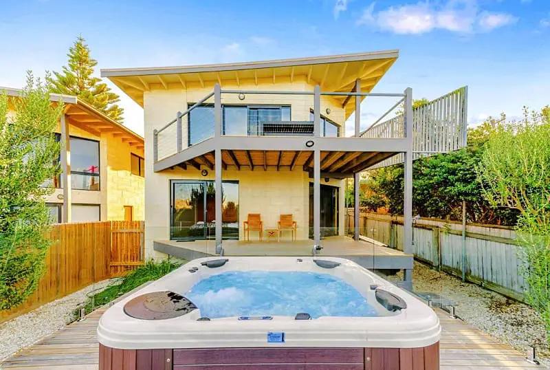 View of the backyard and spa bath at Achilles Apollo Bay accommodation. The two storey building has a verandah and decked area with outdoor chairs.