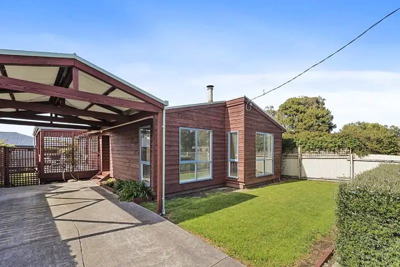 The brown timber Budget By The Bay holiday accommodation with a lush front lawn. 