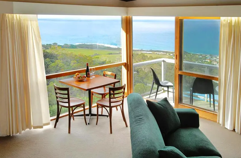 Small table and chairs sitting in the corner of the living room surrounded by windows with ocean views at Chris's Beacon Point Restaurant and Villas.