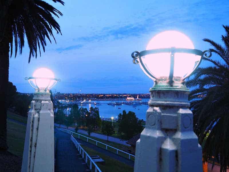 View of Eastern Beach and Geelong Waterfront at night from the top of a path. There are two large old-fashioned round lights glowing in the foreground.