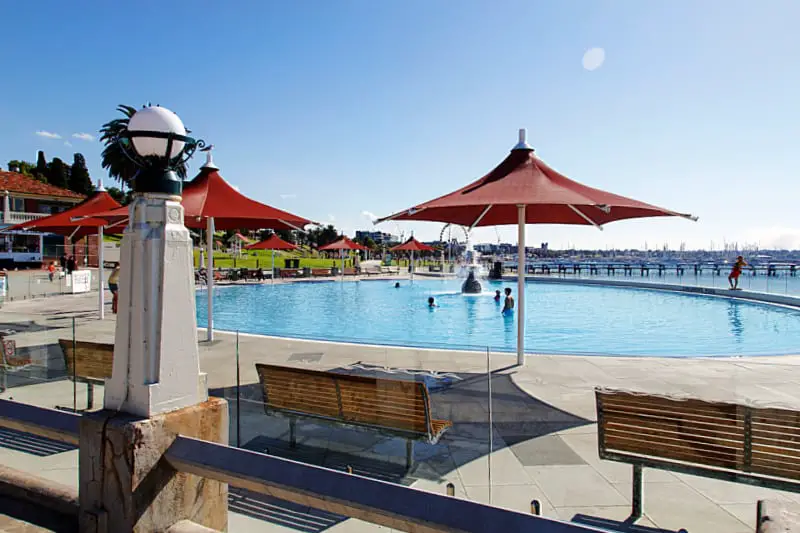 The children's pool at Eastern Beach with umbrellas and seating, a glass enclosure and old fashioned street lights.