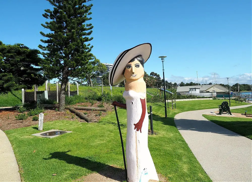 Geelong Bollard of a glamorous woman wearing a pink dress with a large hat and cane standing beside a path.